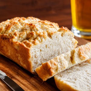 Loaf of Beer Bread with some slices cut with beer in the background.