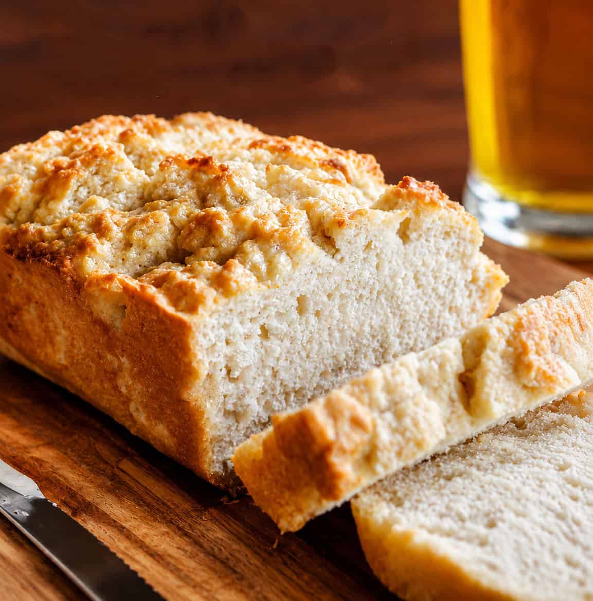 Loaf of Beer Bread with some slices cut with beer in the background.