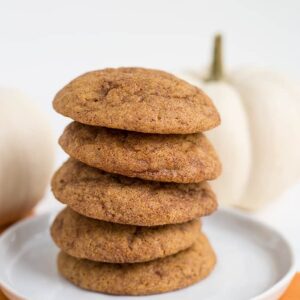 stack of pumpkin snickerdoodles on a white plate with white pumpkins behind them
