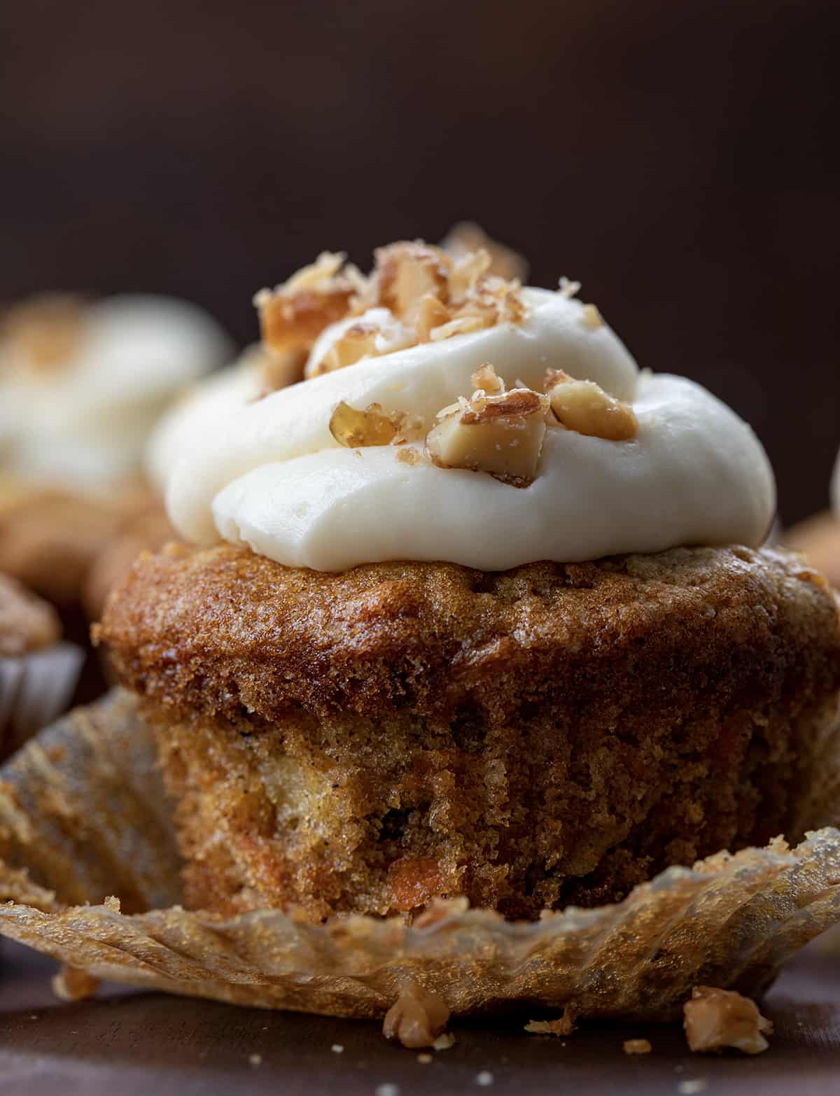 Close up of a Carrot Cake Cupcake with Wrapper Peeled Back and Candied Walnuts on Top of the Cream Cheese Frosting.