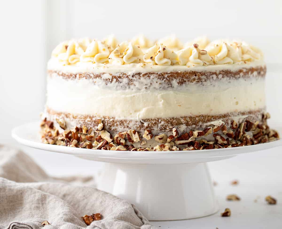 Whole Hummingbird Cake on a White Cake Stand on a Counter.