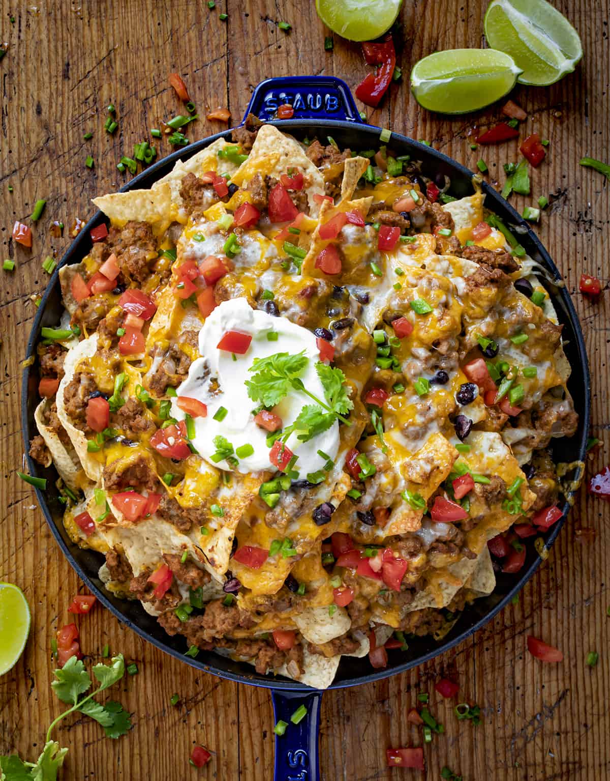 A Skillet Filled with Layers of Beef Nachos and Topped with Melted Cheese, Tomato, Sour Cream, and Lime.