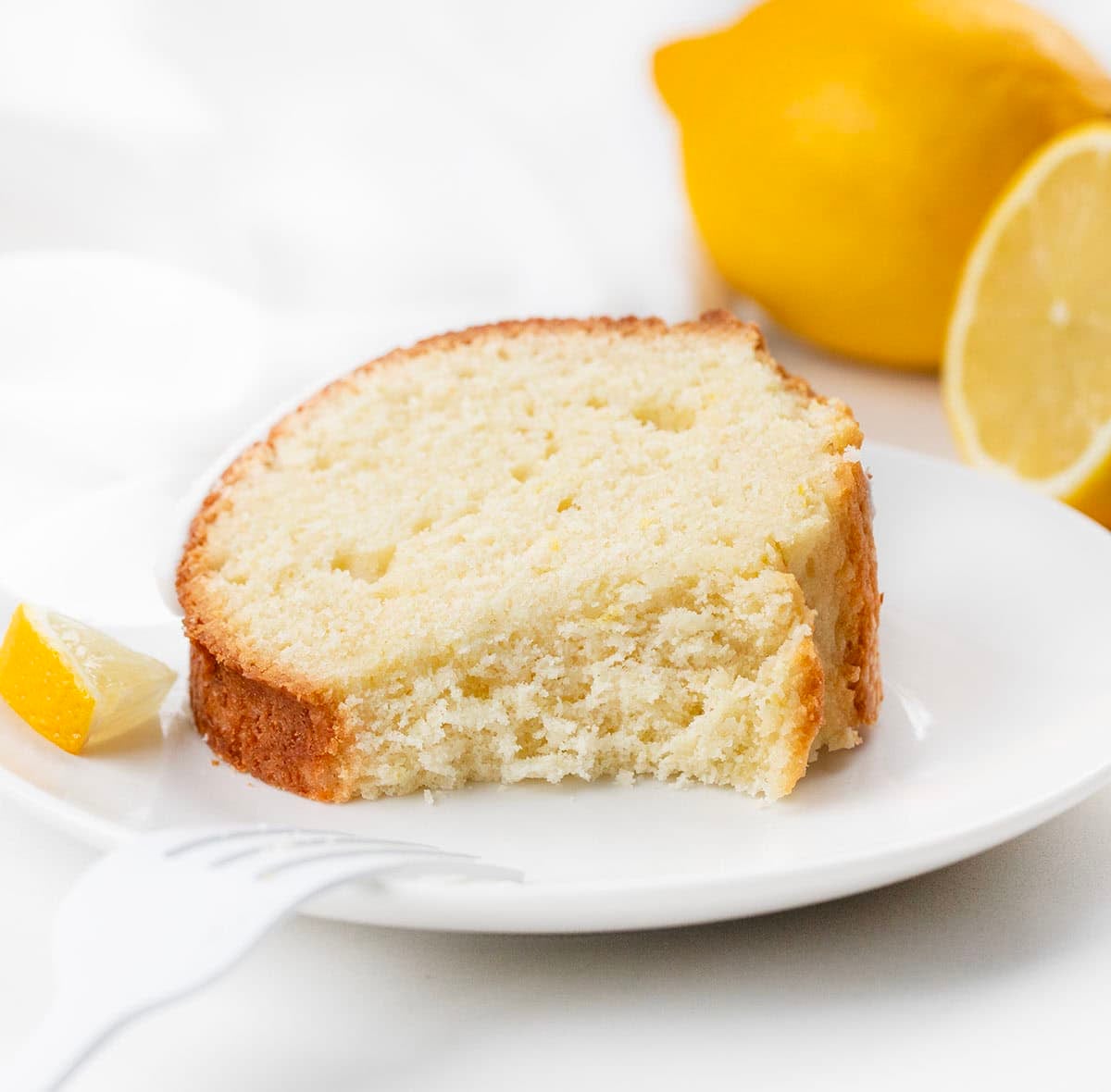 Piece of Lemon Pound Cake on its side on a white plate with a bite missing.