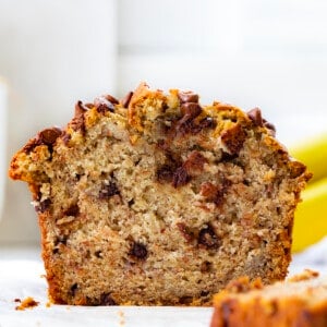Cut into Loaf of Chocolate Chip Banana Bread on a White Counter with Bananas in the Background.