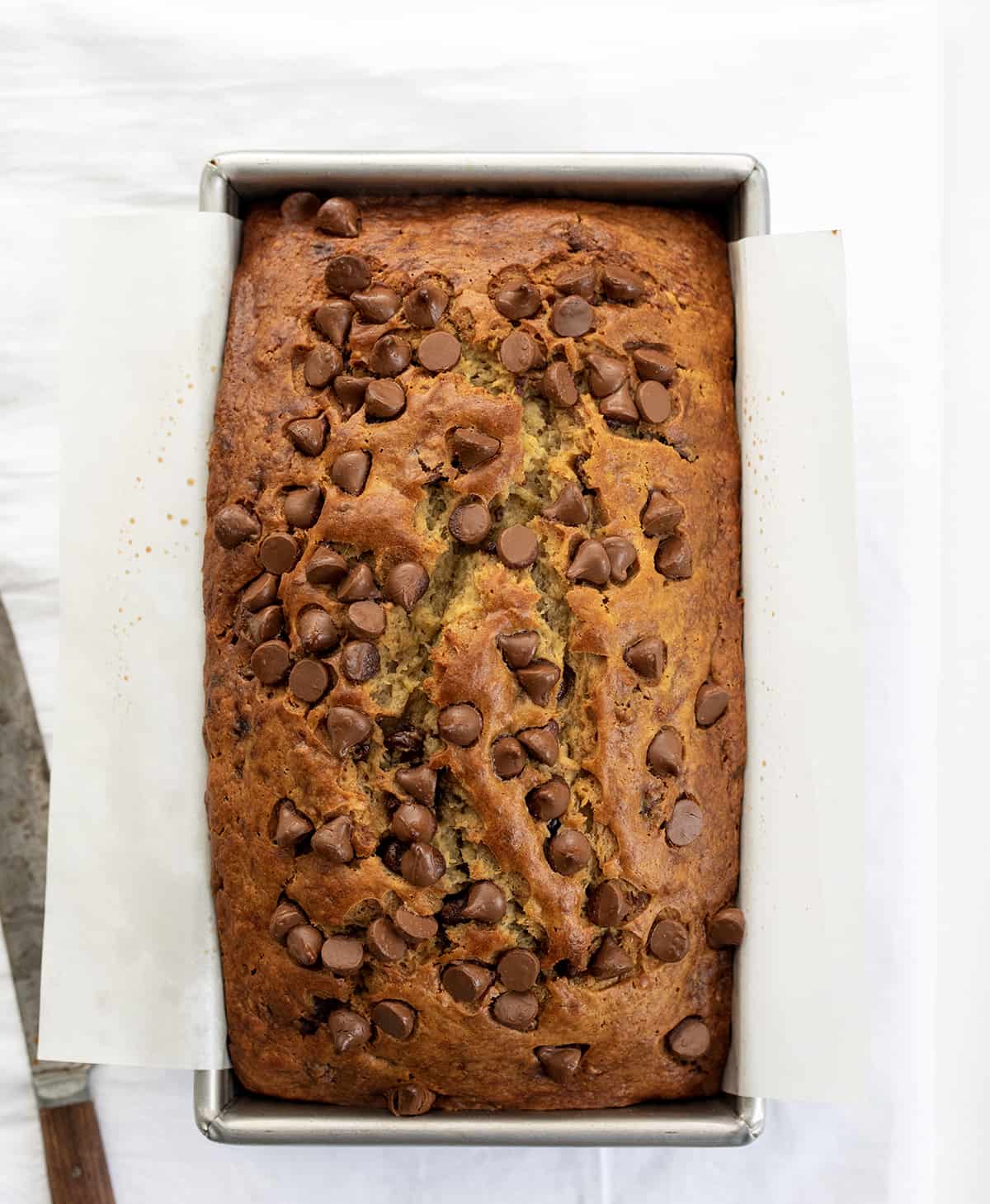 Loaf of Chocolate Chip Banana Bread on a White Counter with a Bread Knife.