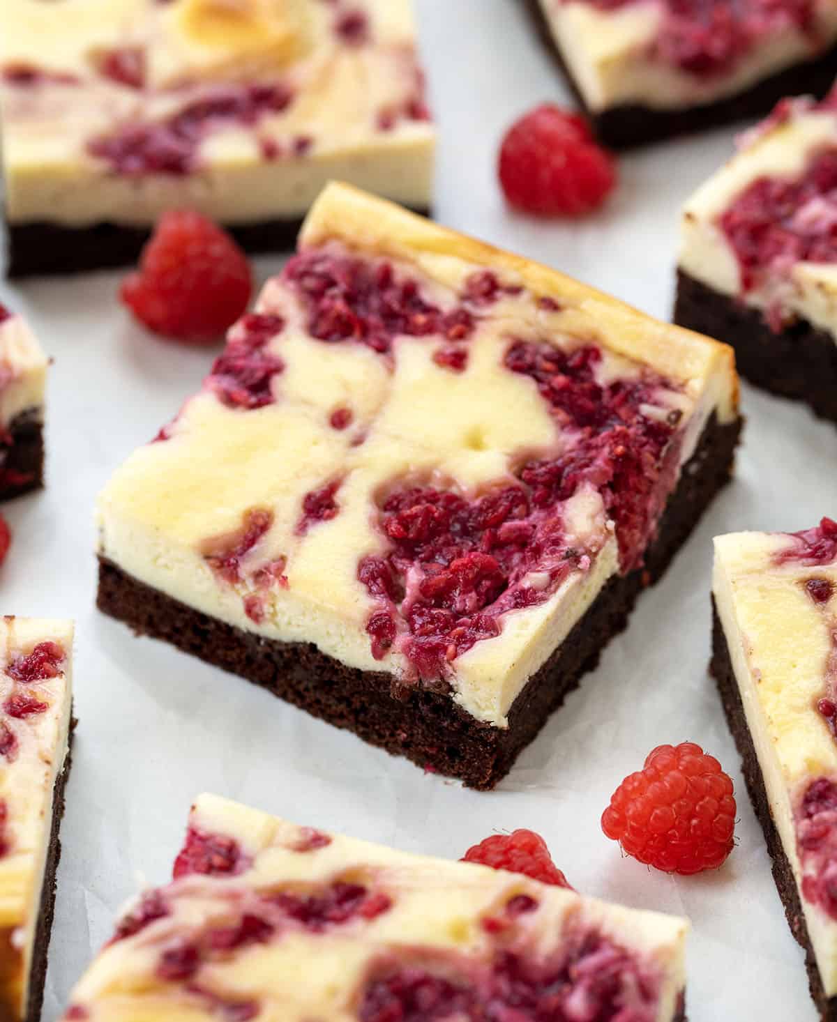 Cut up Raspberry Cheesecake Brownies on a white table with fresh raspberries.