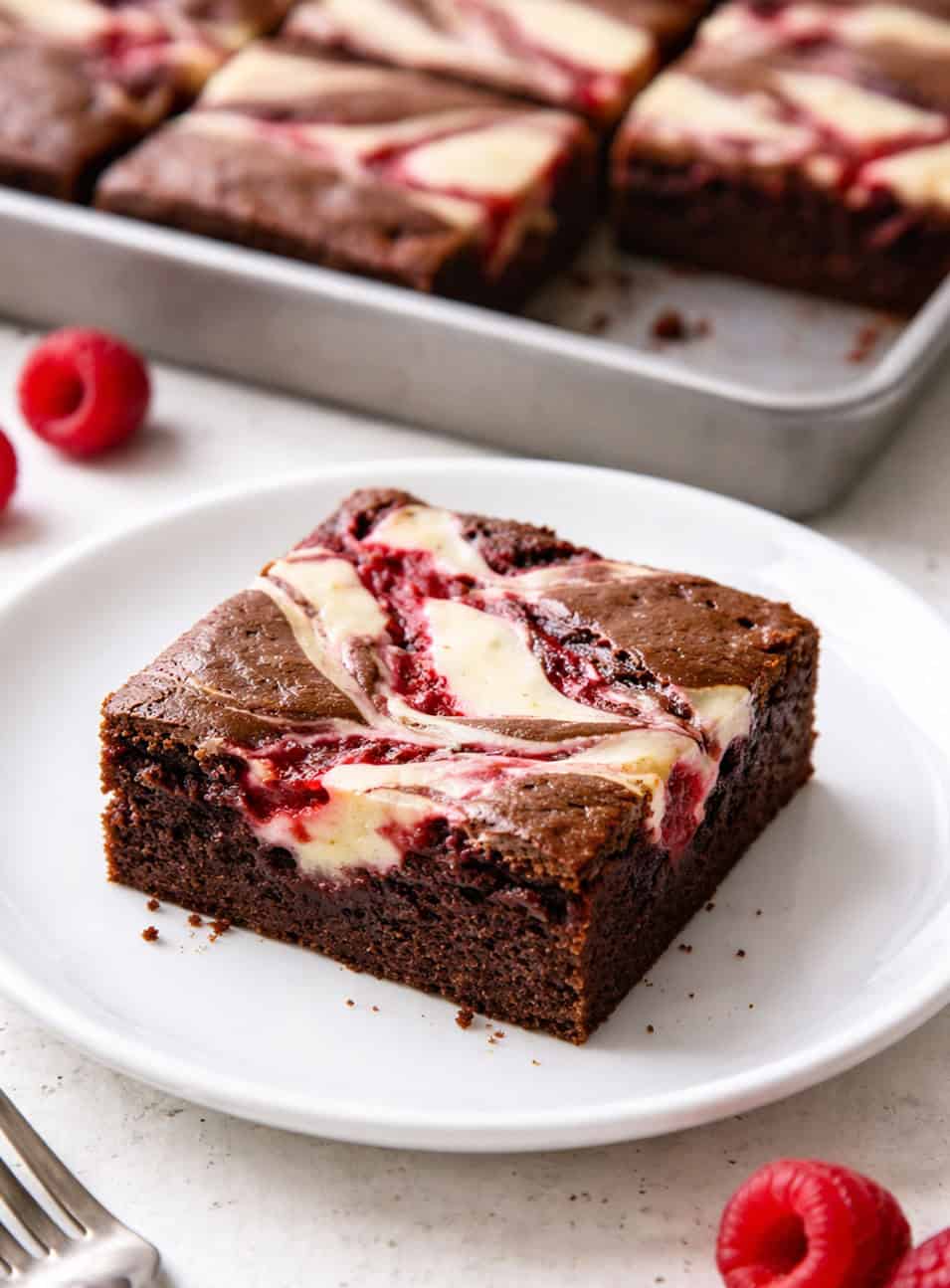 Raspberry Cheesecake Sheetcake slice on a white plate next to the pan.
