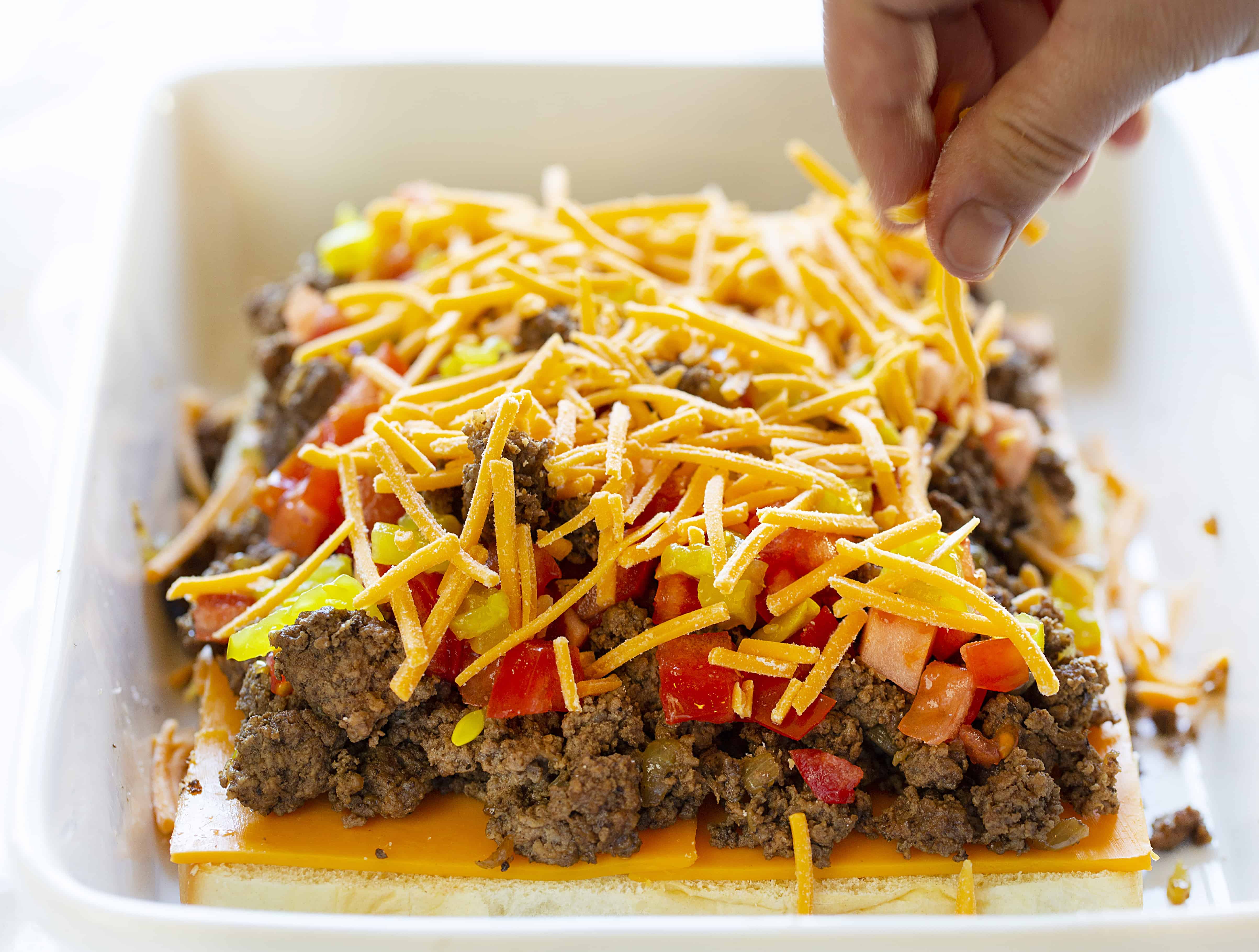 sprinkling cheese layers on a cheeseburger slider