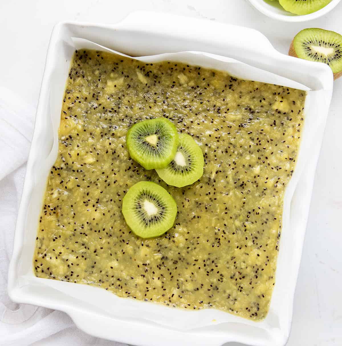 This Kiwi Bars recipe starts with a buttery shortbread crust topped with a smooth, sweet-tart kiwi that sets up perfectly. I like to serve the kiwi bars straight from the refrigerator, nice and chilled. The cool, creamy texture and bright flavor are extra refreshing that way! Pan of Kiwi Bars on a white table from overhead.