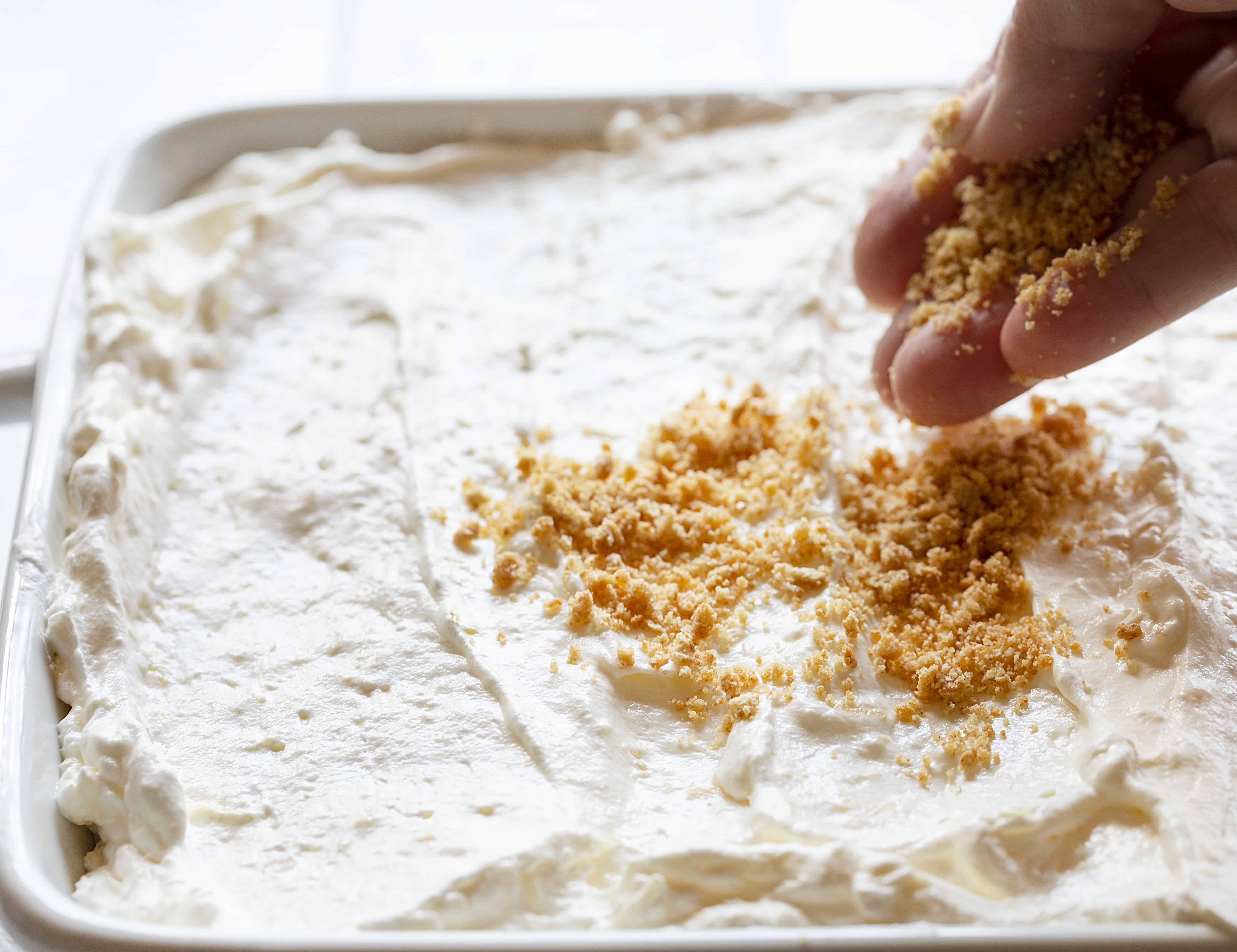 Hand Sprinkling graham cracker crumbs over Easy Pineapple Dessert. 