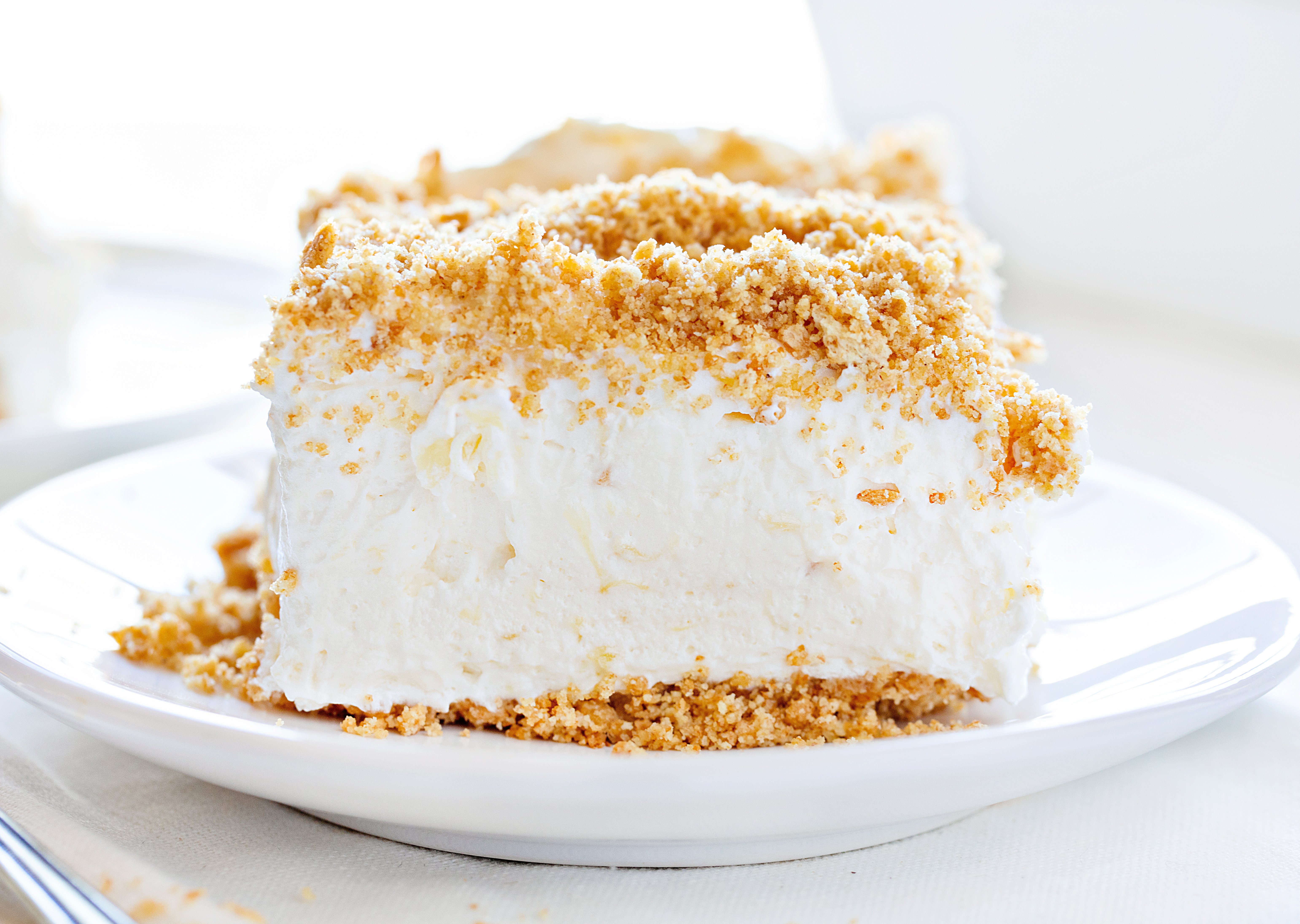 Pineapple Dream Dessert Piece on a White Plate on a White Counter. This dessert is a layer of graham cracker crumbs on the top and bottom and a middle layer of creamy cream cheese pineapple filling.