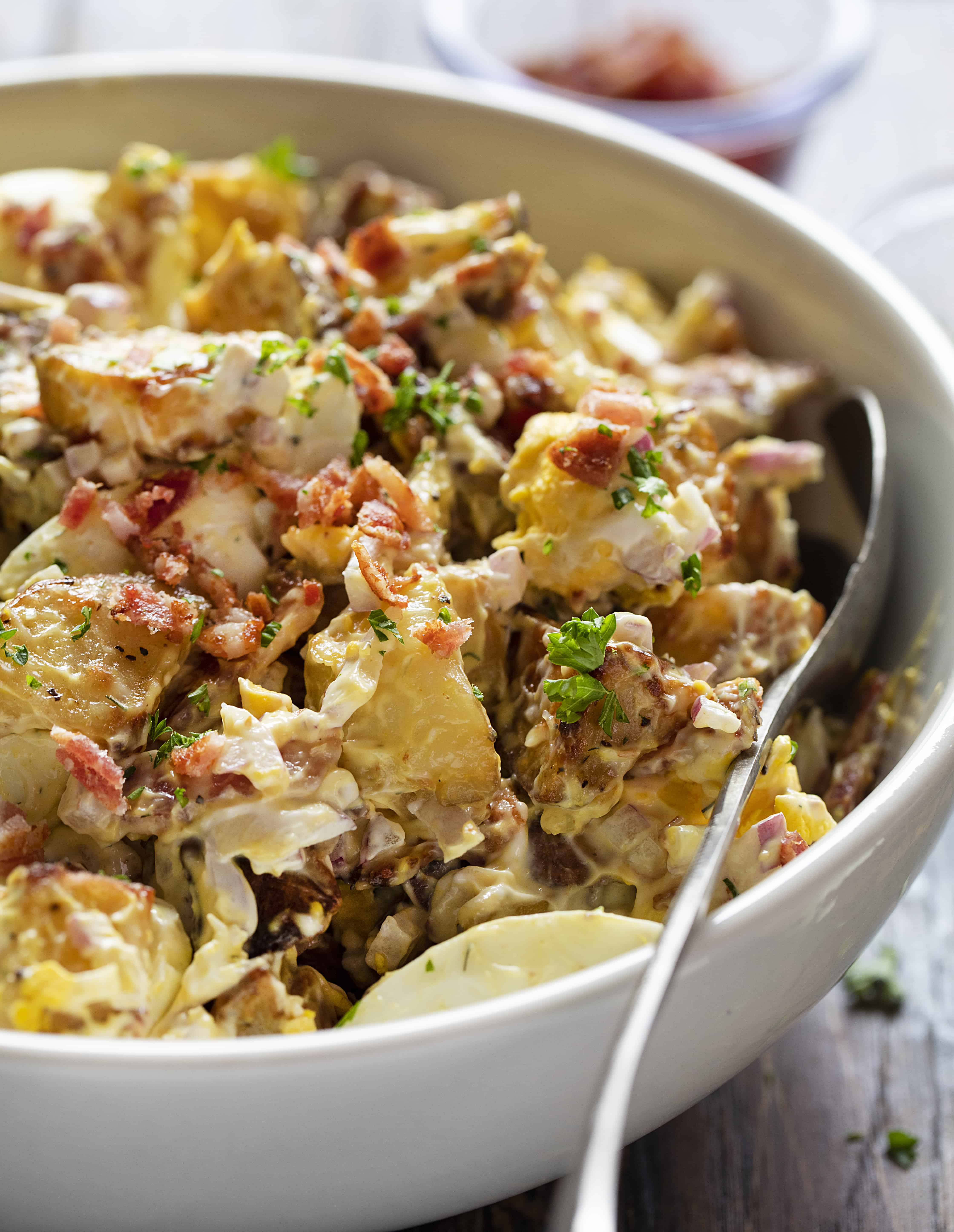 Roasted Potato Salad Salad in a White Bowl with a Close up of the Potatoes, Bacon, and Egg Pieces.