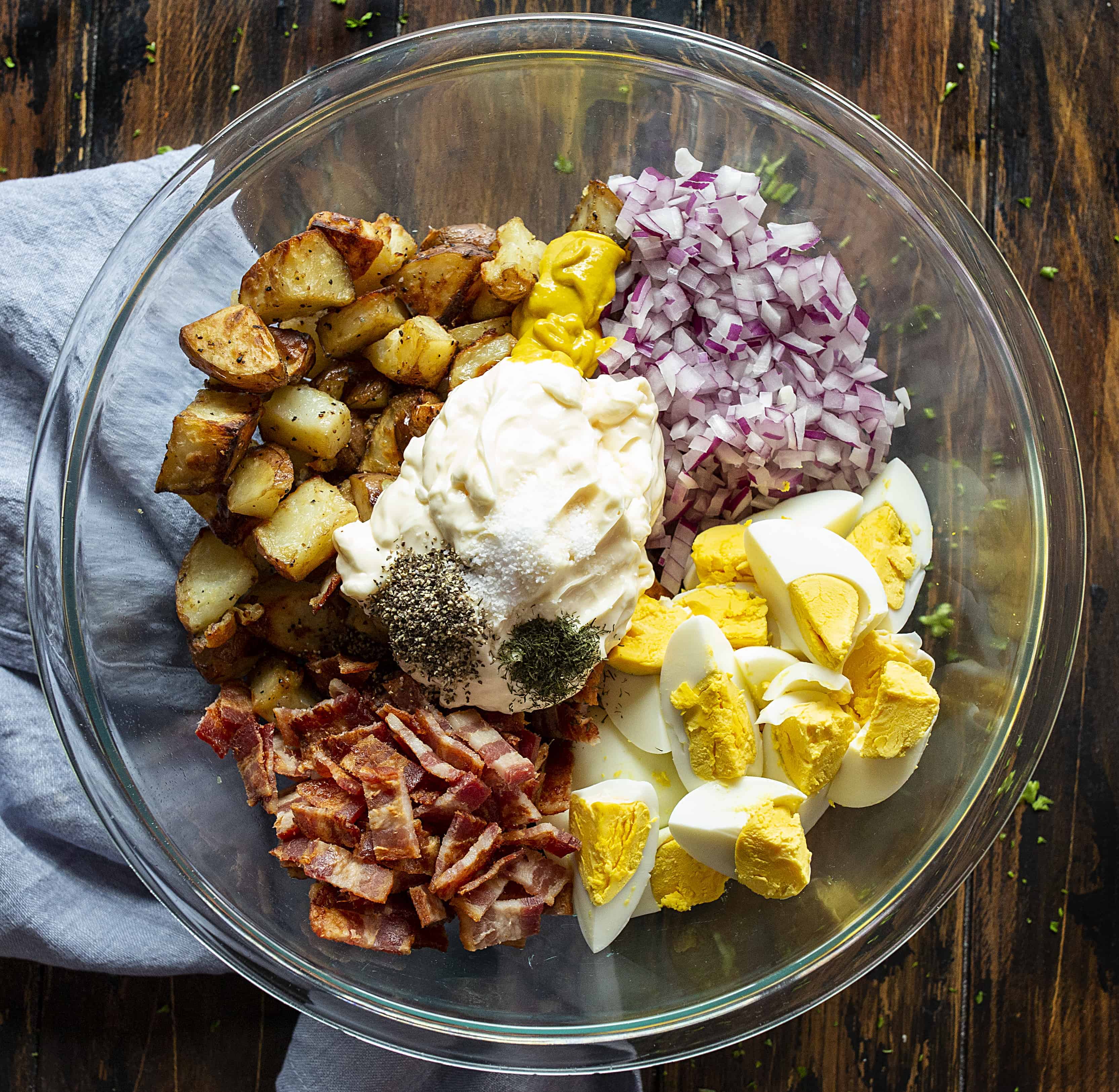 Raw Ingredients for Roasted Potato Salad in a Glass Bowl with Mayo in the middle and Seasonings on Top.