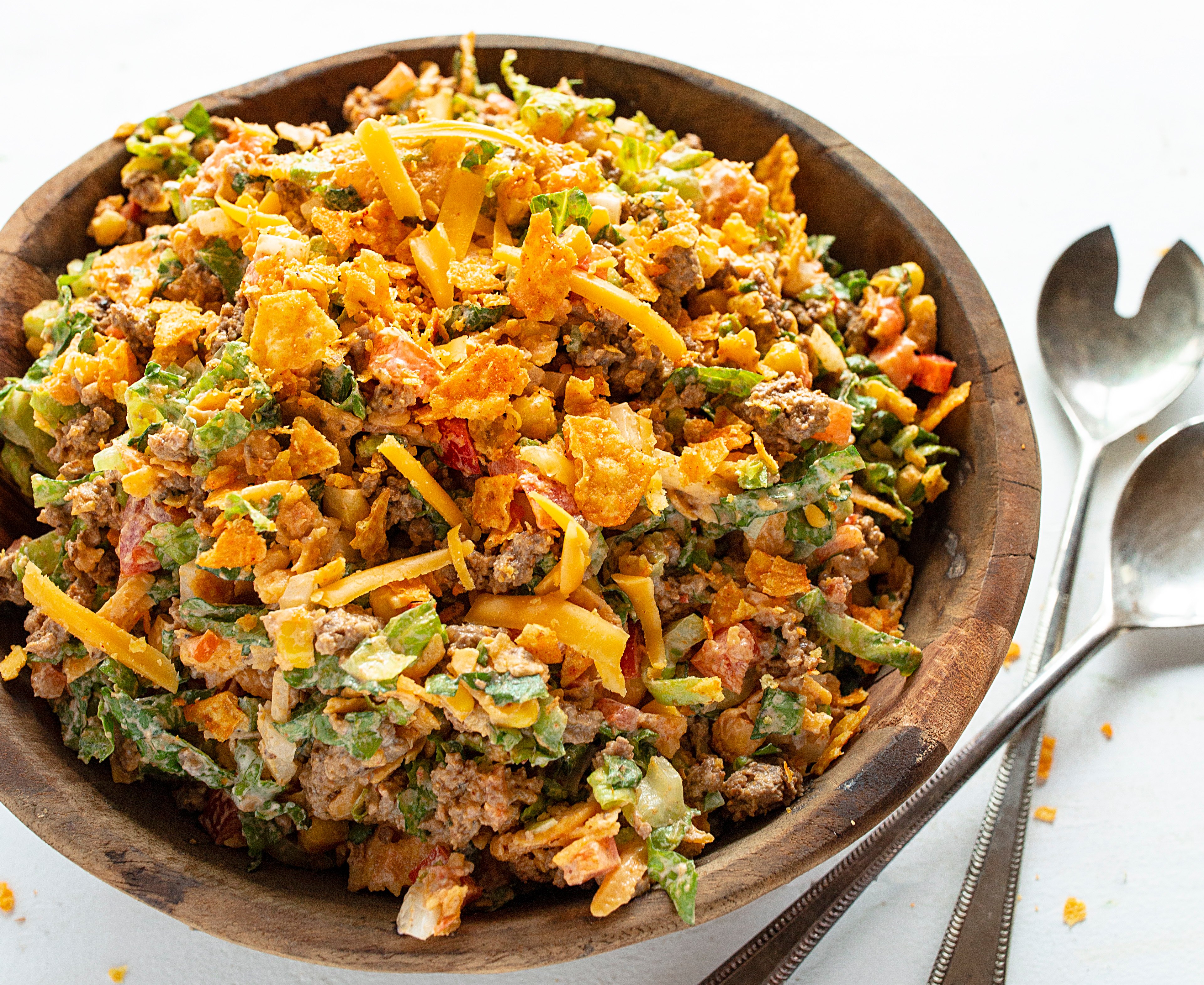 Taco Salad will make taco night a hit in your house again! taco, tacos, taco salad, taco fixings, dorito salad, dorito taco salad, salad, summer salad, summer salad recipes, taco recipes, taco salad recipes, dorito taco recipe, iambaker, i am baker, bbq recipes, cookout recipes, summer recipes, french dressing salad Dorito Taco Salad in a Bowl Kind Of Close Up with Serving Spoons.