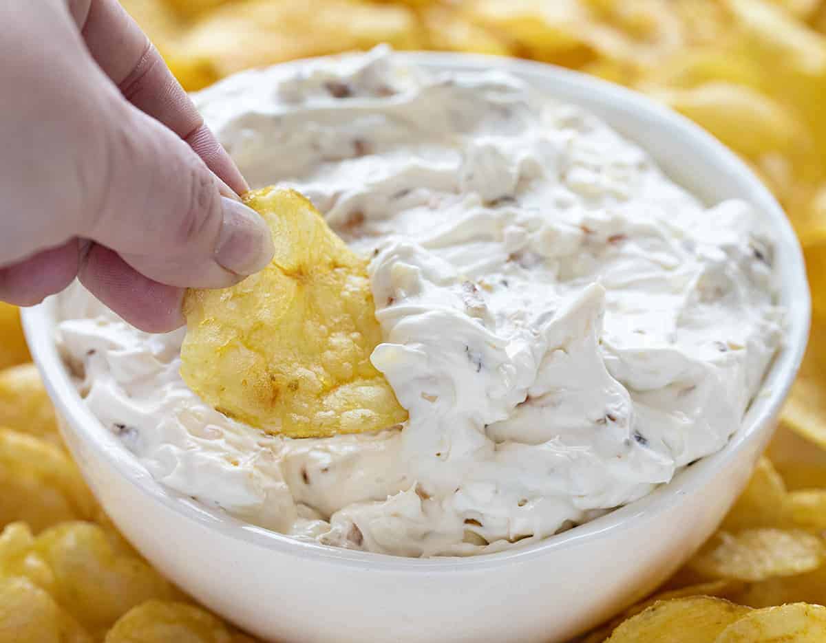 Hand Holding Chip Dipping into Bowl of Caramelized French Onion Dip.
