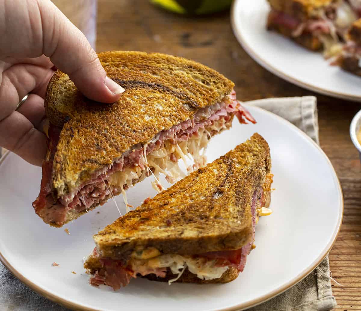 Hand Picking Up a Reuben SandwichOff Ceramic Plate on a Napkin