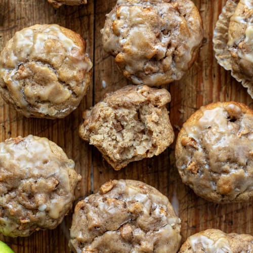 Apples Muffins on a Wooden Cutting Board with One Muffin Halved to Show Inside from Overhead.
