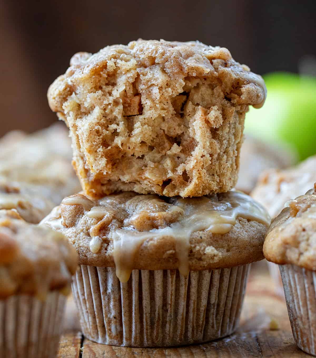 Half Apple Muffin on Top of Another Muffin on a Cutting Board with an Apple in the Back.