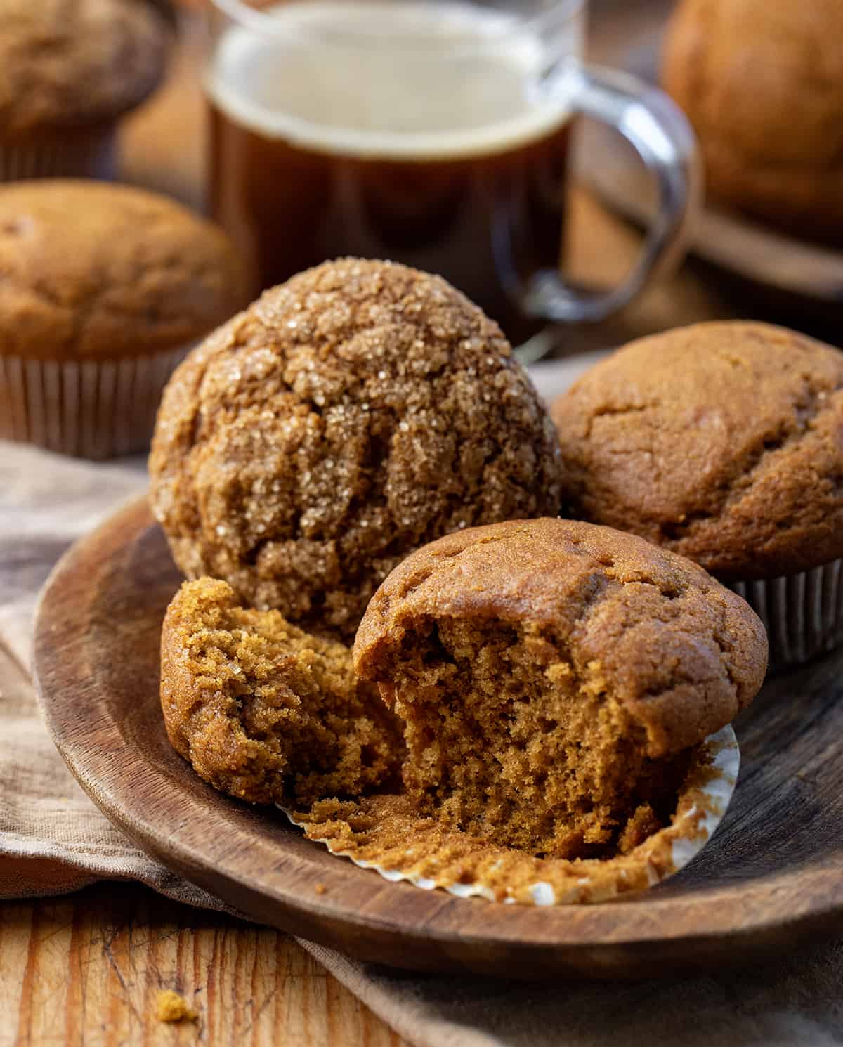 Pumpkin Spice Muffins on a wooden plate with one halved, showing inside texture.