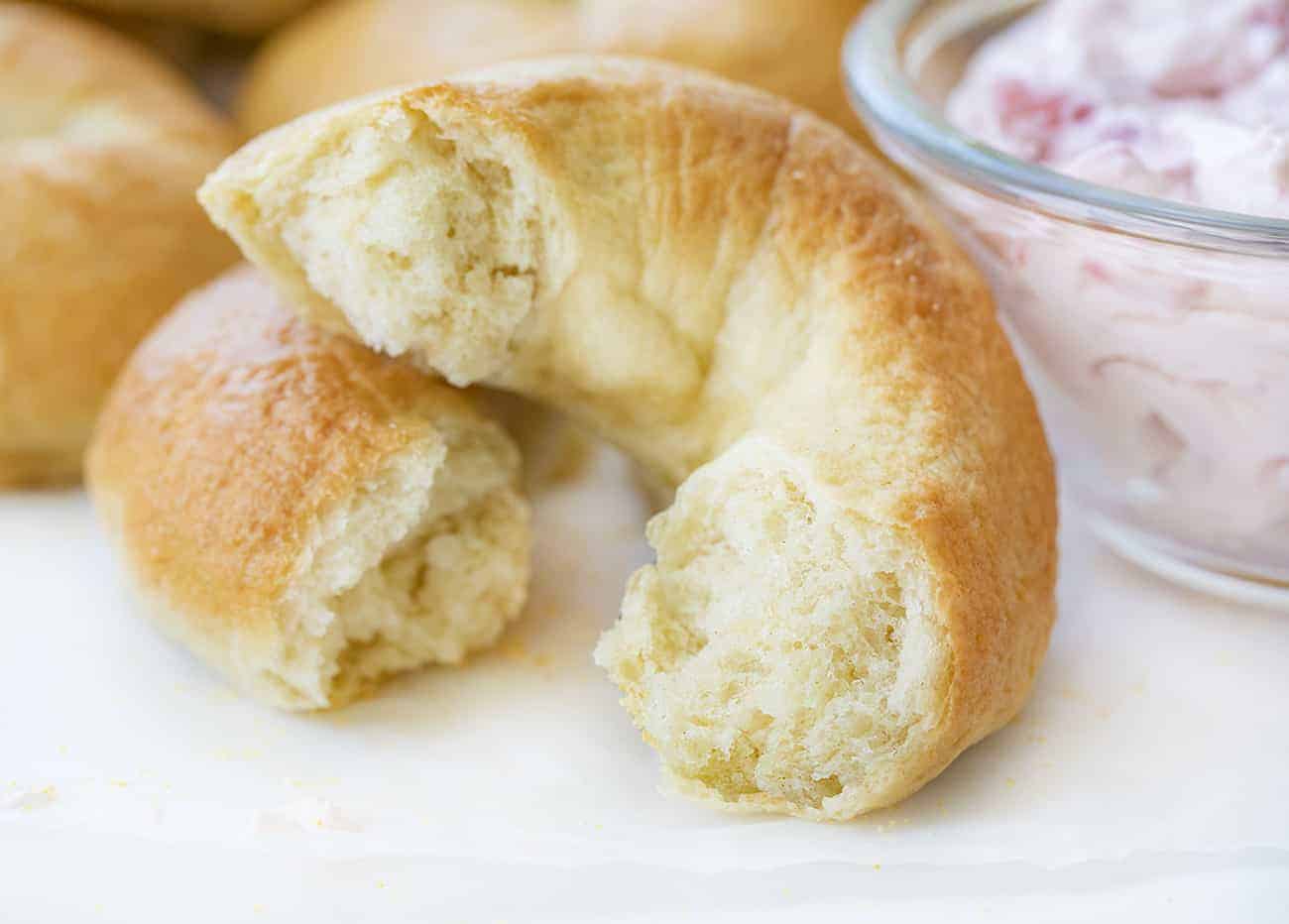 Bagel nature déchiré en deux pour montrer l'intérieur et à côté d'un bol de fromage à la crème aux fraises