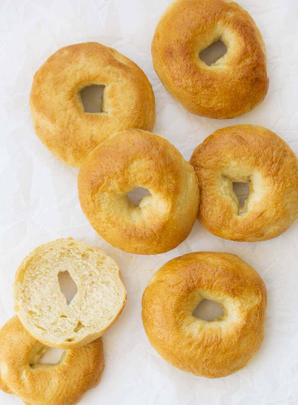 Overhead Image of Plain Bagels on Parchment Paper with one Cut in Half to See Inside