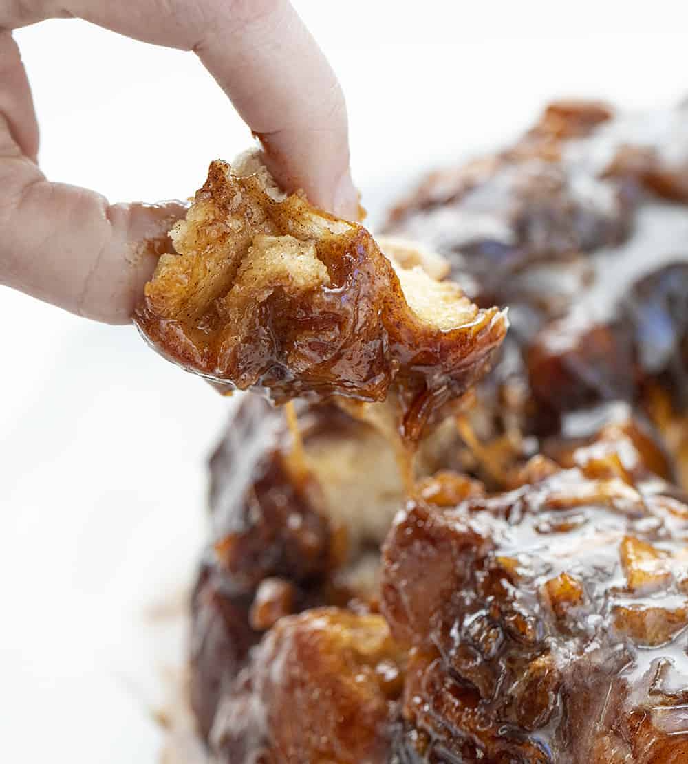 Hand Lifting up a Piece of Layers of Apple Fritter Monkey Bread with Caramel Glaze Pulling Away