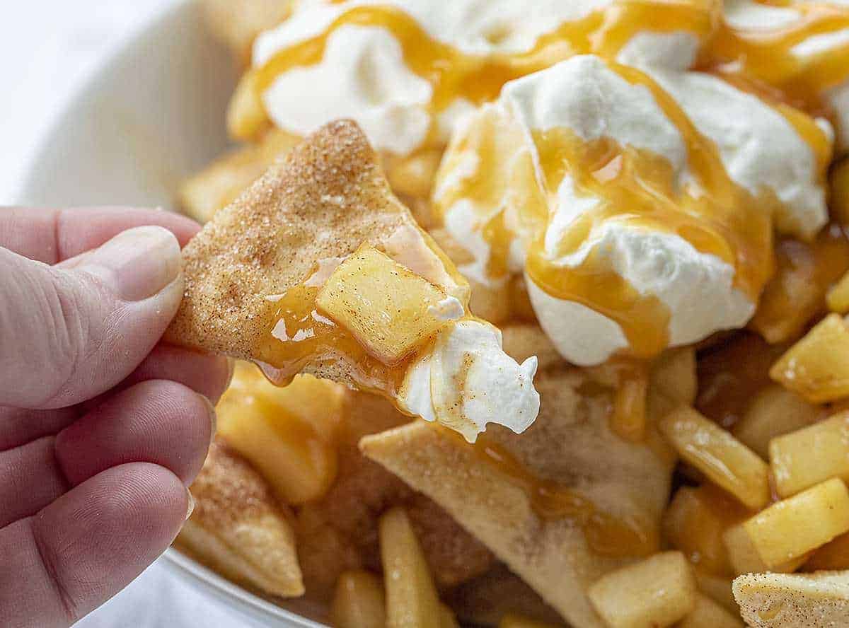 Hand holding One Apple Pie Nacho with apple and whipped cream and caramel on it