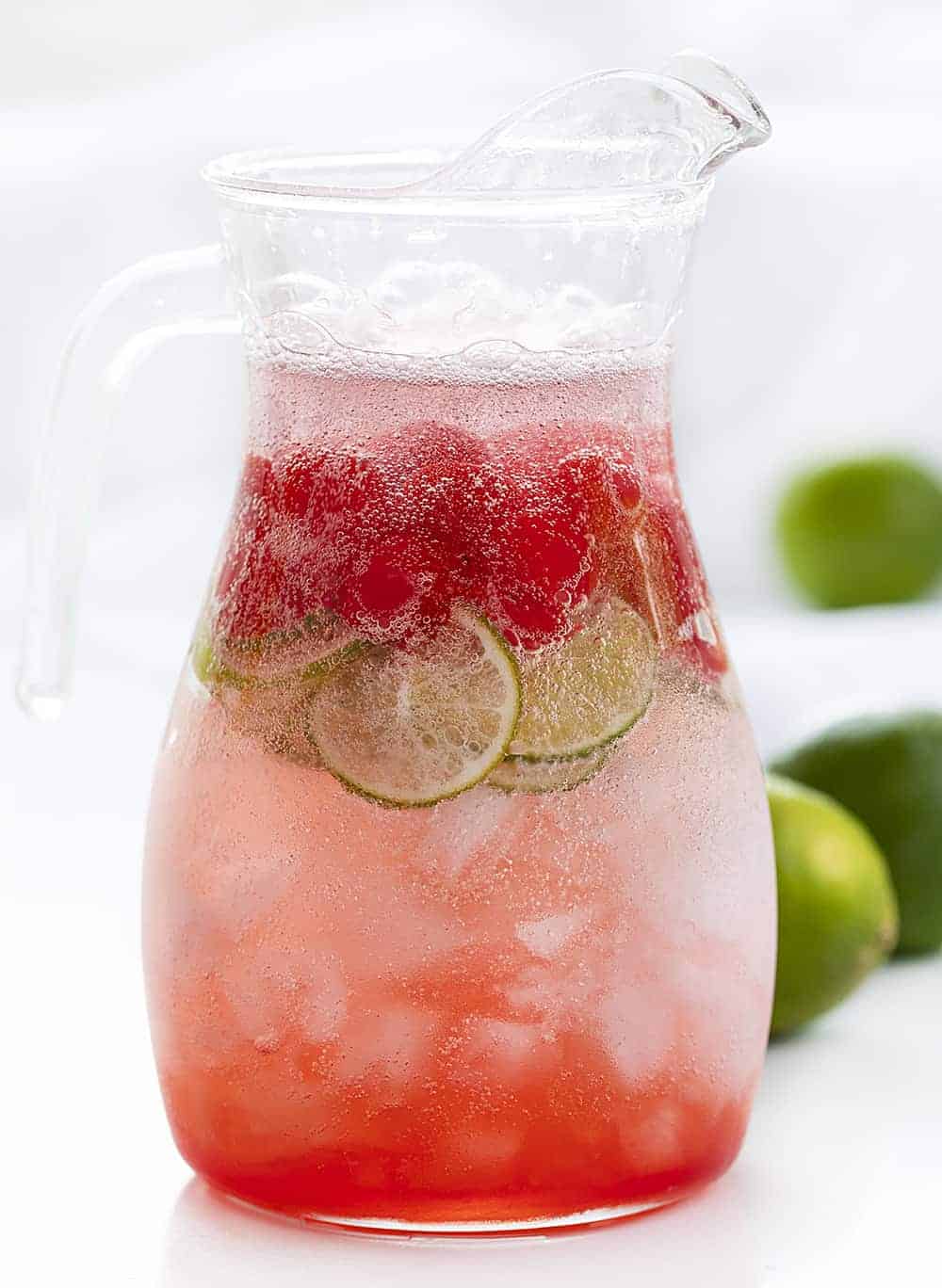 Pitcher of Homemade Cherry Limeade Drink with Fresh Limes in Back