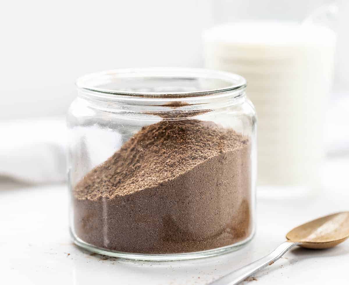 Chocolate Milk Powder in a Jar with a Spoon and Milk in Background