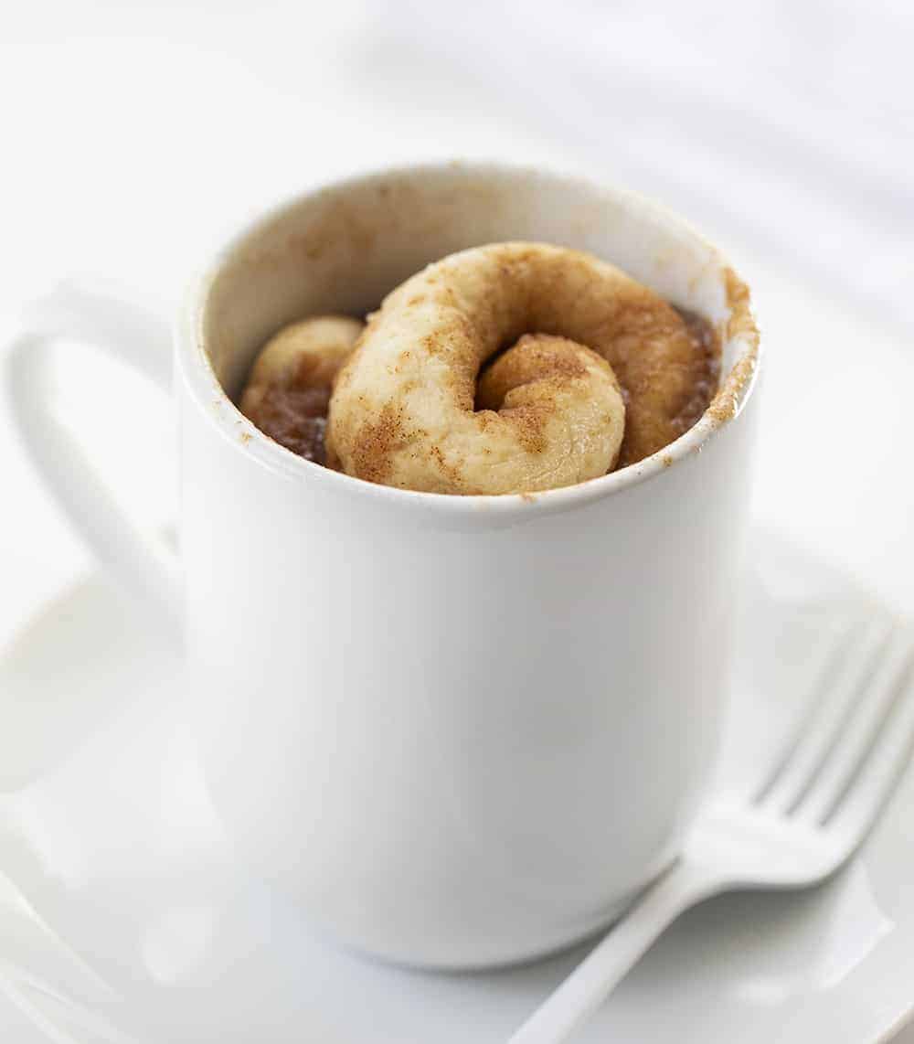 Cooked Cinnamon Roll in a Mug Made in Microwave on White Plate with White Fork