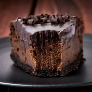 Piece of Chocolate Cheesecake on a black plate with fork impression showing as a bite has just been removed.