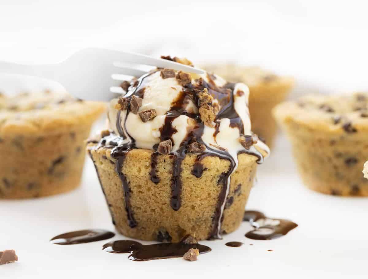 Fork Cutting into a Chocolate Chip Cookie Cup Stuffed with Reese's Peanut Butter Cup and Drizzled with Hot Fudge