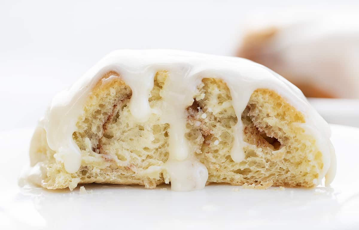 Inside of Cinnamon Roll with Frosting Dripping Over on White Plate
