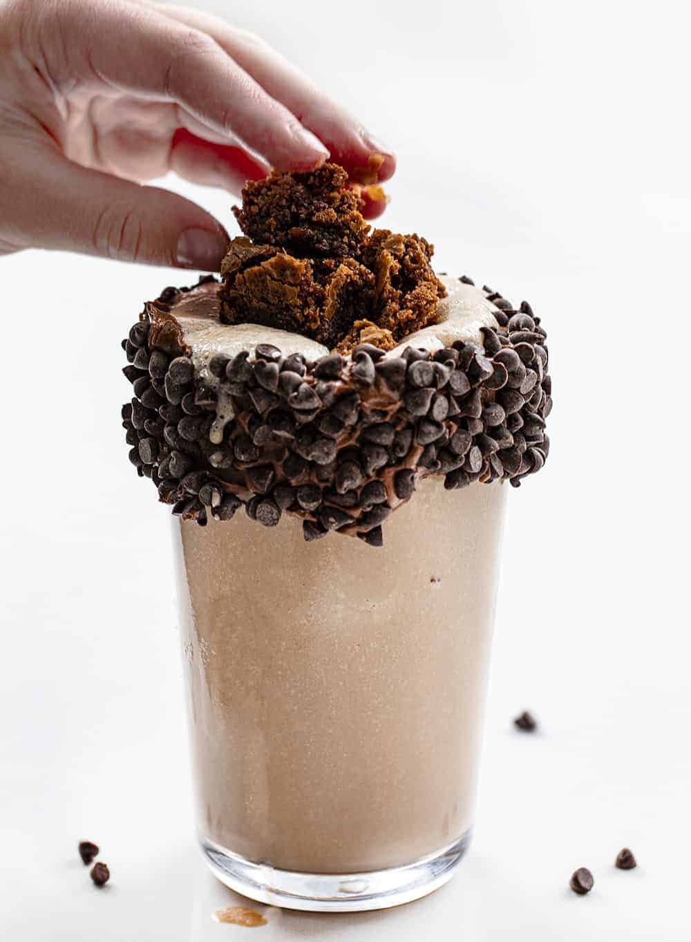 Hand Adding Brownie Chunks to a Glass with Chocolate Milkshake in IT