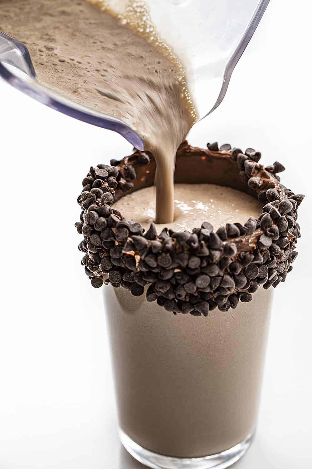 Pouring Chocolate Milkshake into Glass with Chocolate Frosting and Mini Chocolate Chips on It