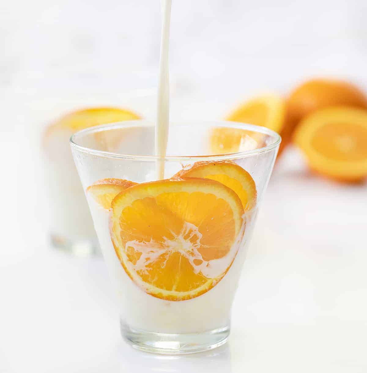 Pouring Milk Into Iced Orange Creamsicle Drink with Oranges in Background