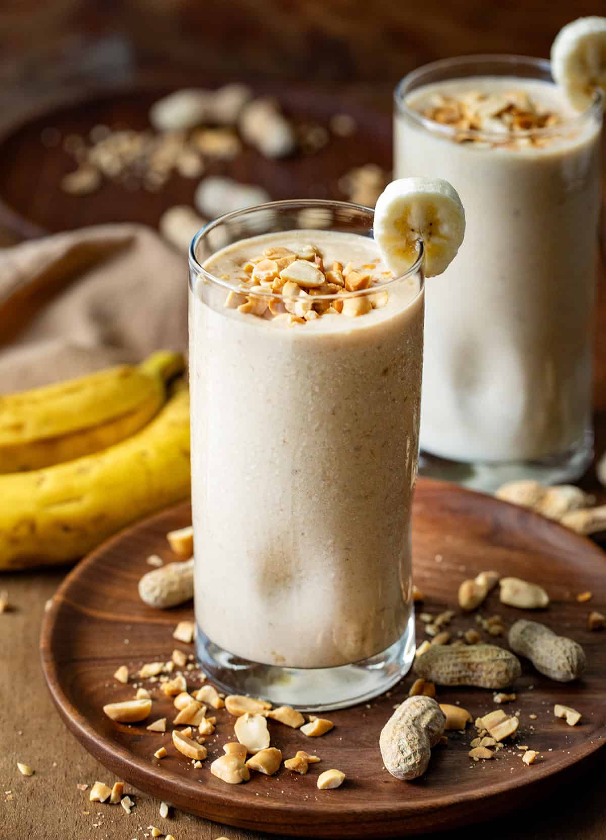 Peanut Butter Banana Smoothie on a dark table with a banana slice garnish and peanuts. 