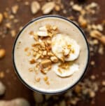 Peanut Butter Banana Smoothie on a dark table with a banana slice garnish and peanuts.