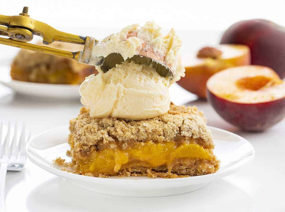 Adding Ice Cream to a Piece of Peach Crisp on a White Plate