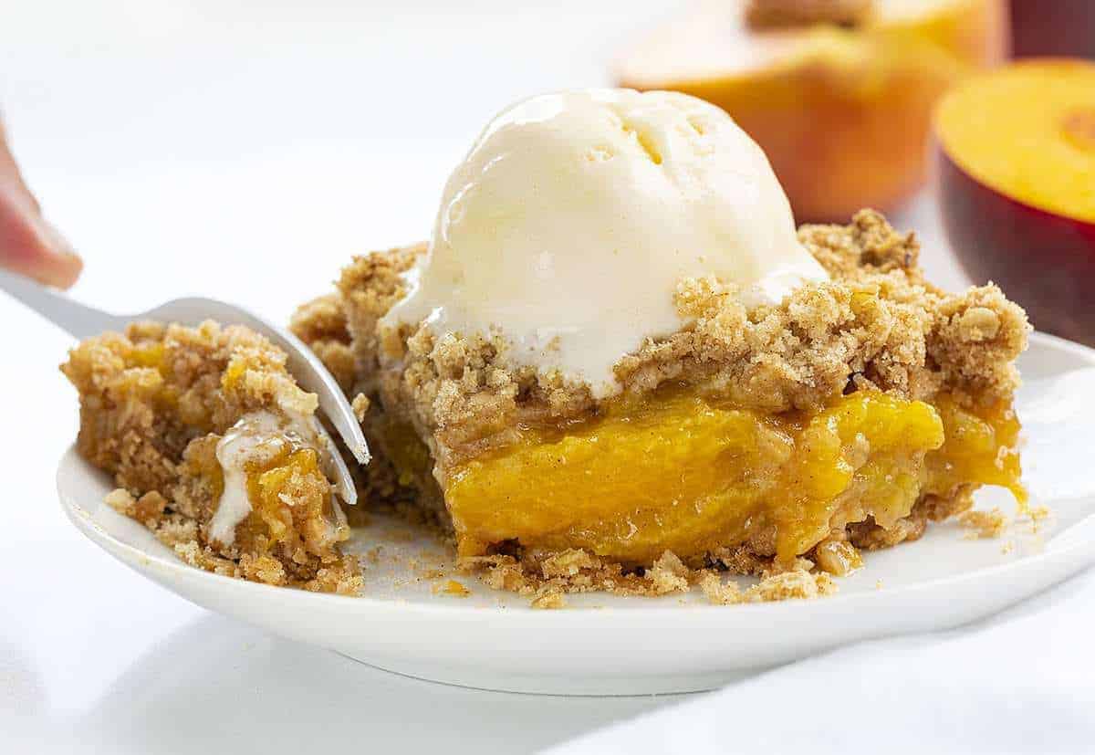 Piece of Peach Crisp on a White Plate with Fork Taking a Bite