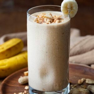 Peanut Butter Banana Smoothie on a dark table with a banana slice garnish and peanuts.