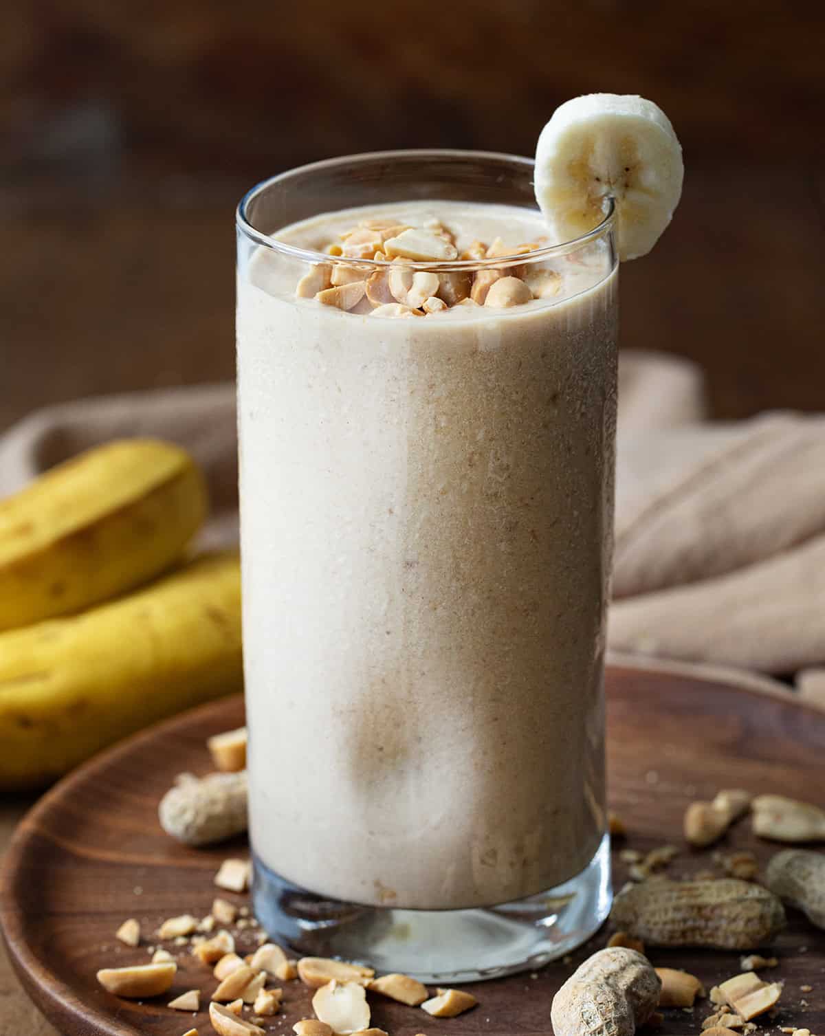 Peanut Butter Banana Smoothie on a dark table with a banana slice garnish and peanuts.