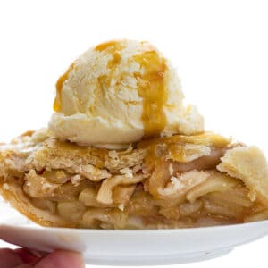 handing holding a white plate of apple pie, topped with ice cream and caramel. apple pie, pies, how to make pie, how to make apple pie, fresh apple pie, fresh fruit pies, how to bake, easy pie, Christmas pies, holiday pies, Christmas baking, holiday baking, Christmas menu, menu planning, hosting, iambaker, i am baker, baking blog