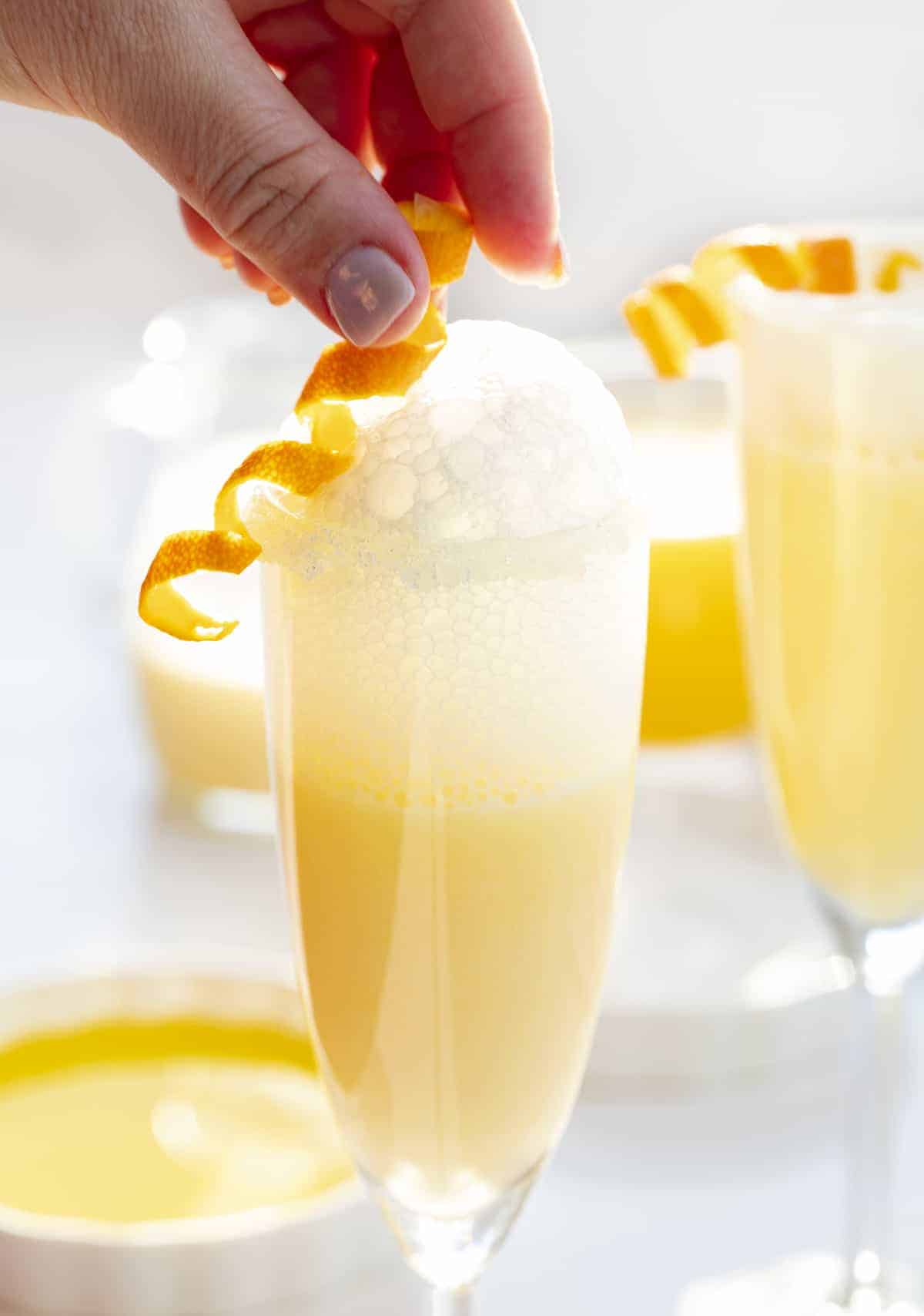 Placing spiraled orange peel garnish on top of creamsicle Prosecco