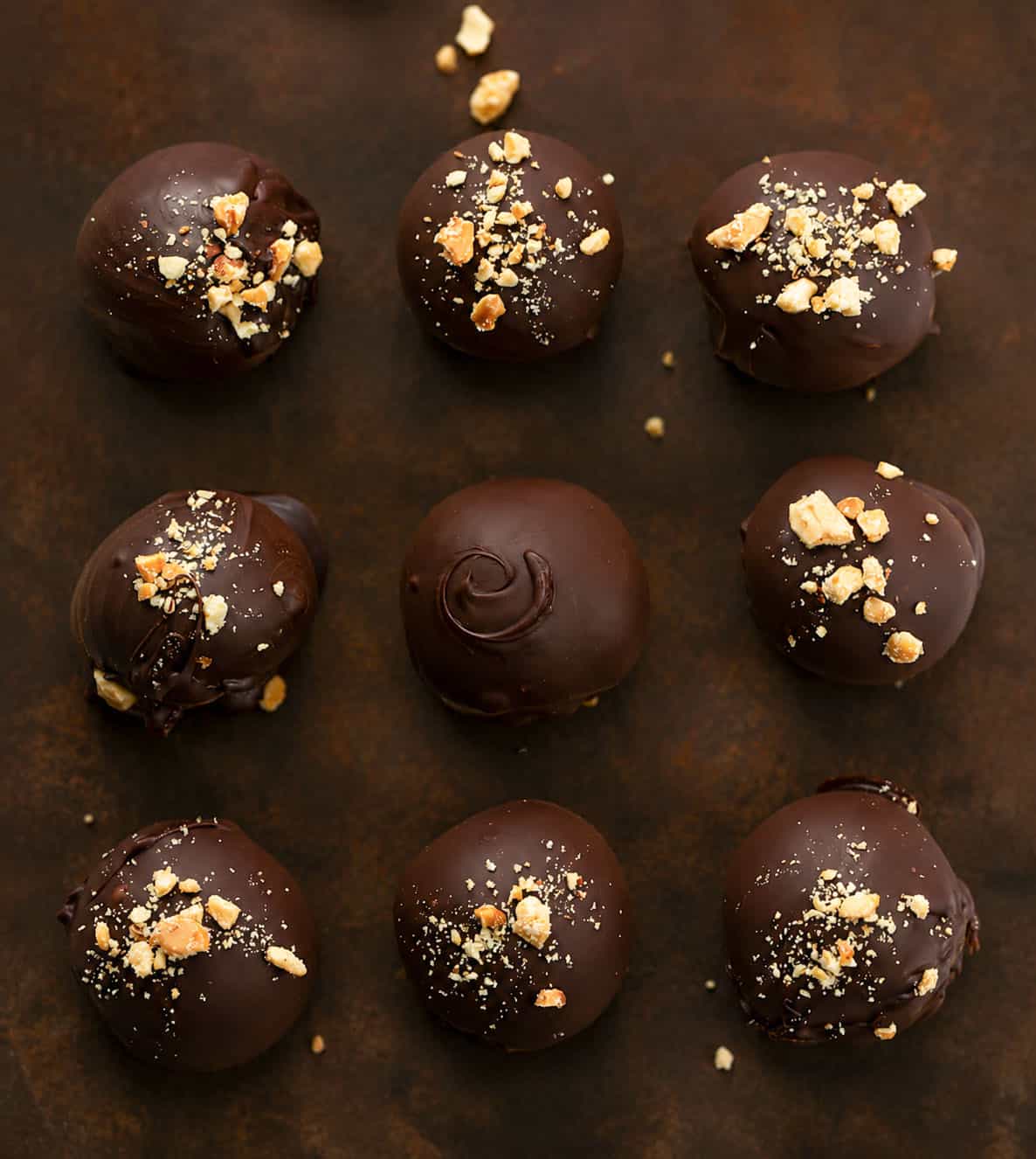 Nine Peanut Butter Balls sprinkled with chopped peanuts on a dark wooden table from overhead.