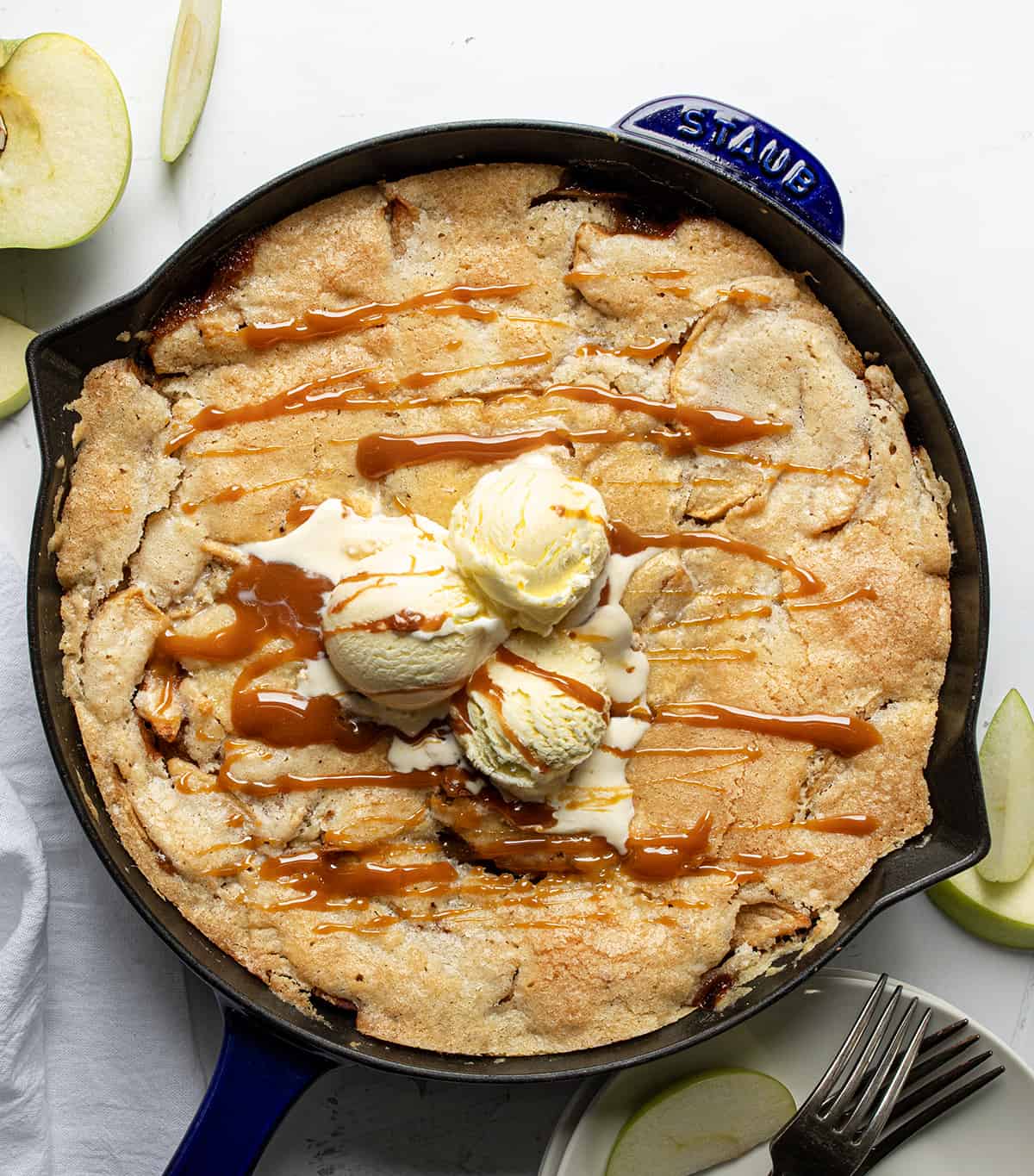 Skillet of Swedish Apple Pie on a White Table With Cut Apples From Overhead.