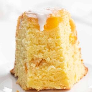 Slice of peach pound cake standing upright with glaze drizzling down the front.