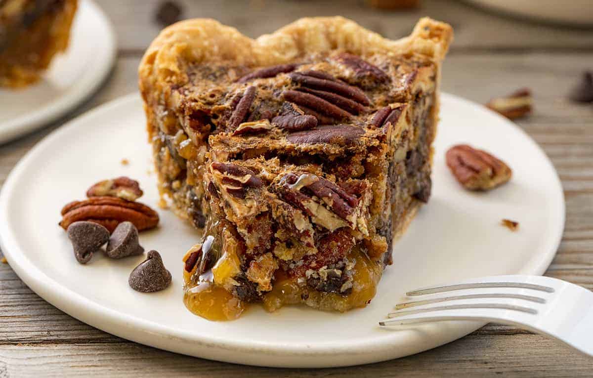 Piece of Chocolate Pecan Pie with Bite Missing and Form on White Plate