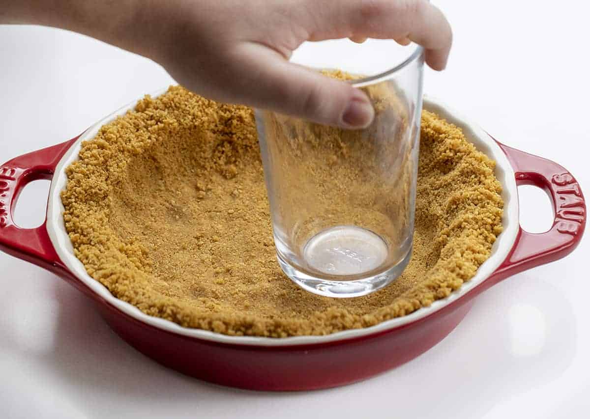 Hand Pressing Down Graham Cracker Crust with a Glass