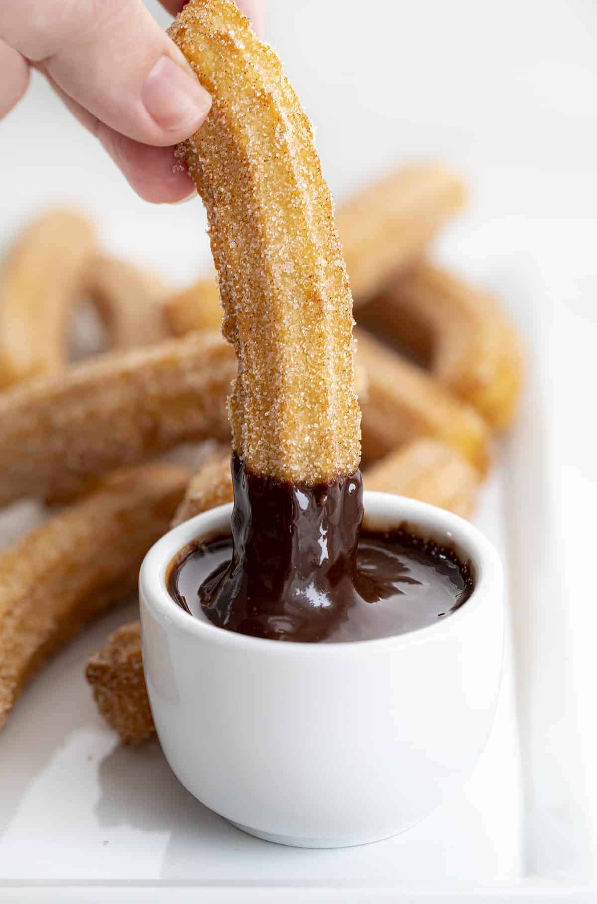 Churros are dough that is piped into hot oil, fried, and then rolled and coated in a cinnamon and sugar mixture. How to Fry Churros, Churro Recipes, Air Fryer Churros, Quick Churros, How to Make Churros, Dessert, Snack, recipes, baking, i am baker, iambaker Dipping Churro Into Chocolate